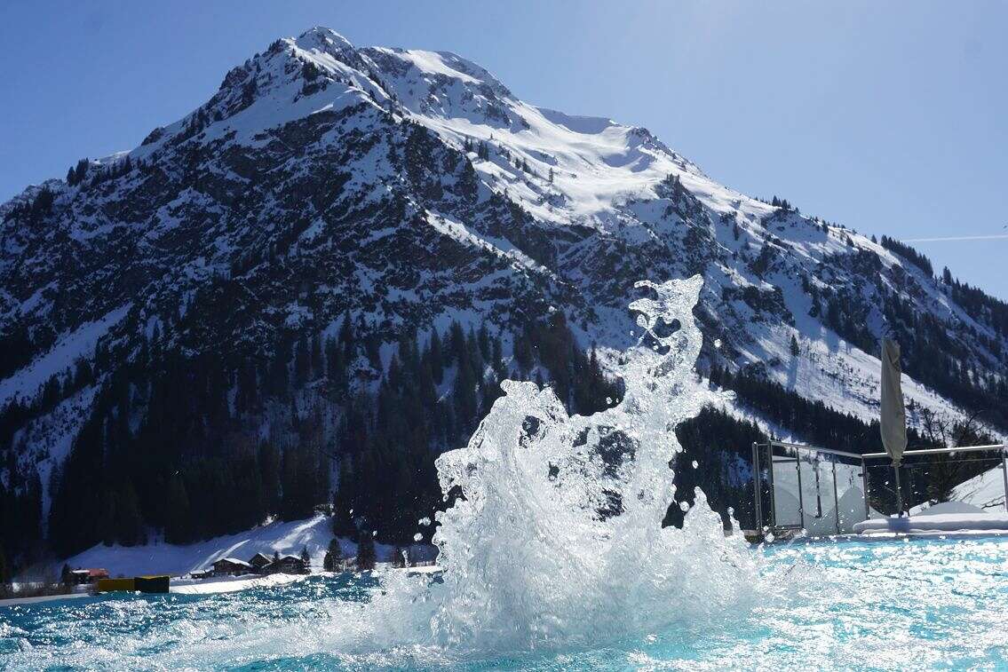 Schwimmen im Außenpool des Rosenhofs mit Blick auf die schneebedeckten Berge.